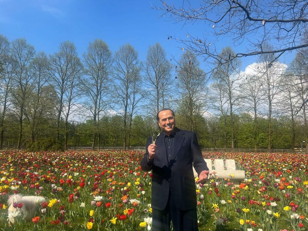Silvio Berlusconi se trouve dans un jardin entouré de fleurs colorées, capturant un moment de calme et de contemplation. Sa posture détendue et son regard bienveillant témoignent de sa passion pour la beauté de la nature et révèlent une facette plus douce de sa personnalité politique.