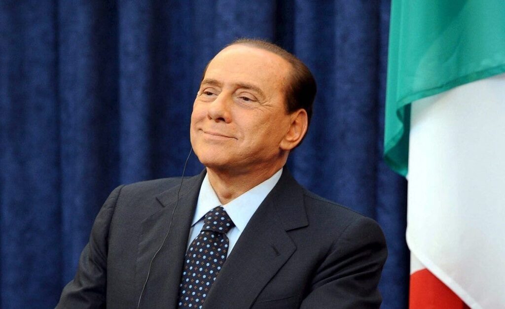 Silvio Berlusconi, l'ancien Premier ministre italien, se tient avec assurance lors d'un rassemblement politique, s'adressant à une foule avec son charisme caractéristique et ses gestes expressifs.